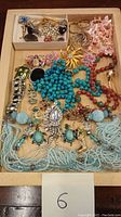 Full view of assorted costume jewelry lot laid out on a wooden tray showing necklaces, rings, earrings, and brooches in various colors and styles.