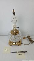 Cut crystal and brass table lamp with attached electric cord and on/off switch and a sterling silver letter opener placed in front.