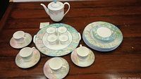 Full set displayed on wooden table showing teapot, cups, saucers, and plates arranged in groups.