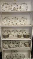 Shelf with multiple shelves showing full set of Johann Haviland china including plates, bowls, covered casserole, gravy boat, cups and saucers arranged for inventory photography.