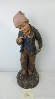 Full view of chalkware boy figure with detailed paint and clothing, standing on round base with visible paint wear.