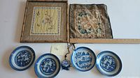 Photo showing four blue and white Canton dishes, two framed needlework pieces, one blue and white ceramic pendant with black beaded necklace chain, and a wooden ruler for scale.