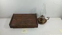 Wooden lap desk and brass hurricane lamp side by side on a white surface.