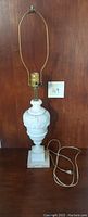 Front view of vintage white marble table lamp with brass socket and harp holder against a wooden background, small card labeled '49' next to lamp