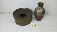 Vintage brass spittoon and enamel decorated metal floral vase side by side.