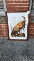 Full view of the framed Wild Turkey print against a brick wall, wood frame visible.