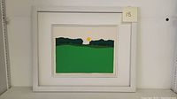 Framed woodblock art print showing minimalistic green field landscape with a setting sun, mounted on white mat, surrounded by white frame.
