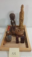 Lot showing all wooden items placed on wooden tray: carved figures, circular box with lid, small statues, and wooden staff or rod.