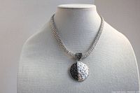 Front view of silver-tone multi-strand chain necklace with black and white circular rhinestone-studded pendant on a mannequin.