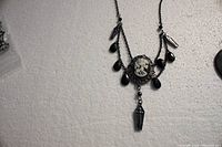 Photo of black chain necklace showing white skeleton cameo with black bead drops and hanging coffin pendant.