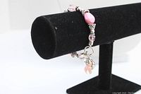 Photo of the elastic Breast Cancer Awareness bracelet displayed on a black velvet stand, showing pink beads and charms.