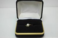 Ring shown in black velvet ring box with cream interior and gold trim, showing pearl and gold band.