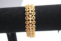 Close-up photo of gold tone lacey bracelet featuring small pearl beads on a black display stand.