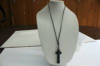 Full view of black cross pendant hanging on leather cord displayed on necklace stand
