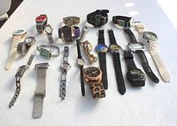 Wide view of 18 wrist watches arranged on a flat white surface, showing diverse styles, bands and face designs