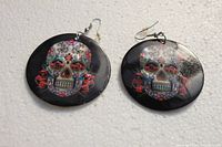 Pair of black large round earrings with colorful sugar skull designs attached to fishhook wires, shown on white background.