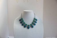 Front view of the Lia Sophia statement necklace on bust stand showing eleven large cabochons alternating in three shades of green and teal with clear rhinestones.