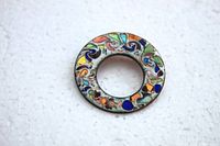 Top view of circular copper brooch with multicolor enamel swirl pattern against white background.
