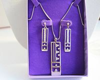 Silver tone necklace with rectangular rhinestone pendant and matching pierced earrings displayed on purple background inside original box