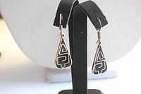 Pair of triangular sterling silver earrings with black enamel and geometric design, displayed on earring stand.