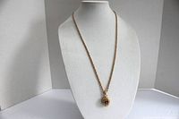 Full view of the gold tone necklace with chain and pendant displayed on a bust