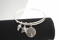 Silver tone adjustable bracelet displayed on a black velvet roll, showing the three charms: Earth Angel tree charm, star charm, and wing charm.