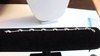 Sterling silver bracelet laid flat on black cushion, showing wire-link style with round accents and clasp