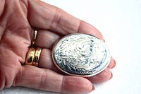 Hand holding the oval etched sterling silver brooch showing size relative to fingers and details of etching.