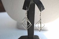 Pair of silver drop earrings with three intertwined squares each, hung on black stand.