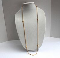Front view of the vintage gold tone long chain necklace displayed on a bust stand showing the full length and the spaced round ball accents.