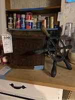 Antique Japanese wooden tea box and antique machinery steering wheel on wooden shelf with various items in background.