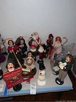 Wide view of 13 Byers Choice Christmas Caroler figurines, some with accessories including Santa, snowman, and musicians, arranged on table.
