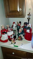 Wide shot showing all nine Byers Choice Christmas Caroler figurines arranged on a white countertop beneath a wooden cabinet.