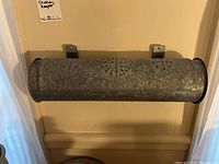 Front view of the punched tin metal candle keeper hanging on the wall, showing its cylindrical shape and mounting brackets.