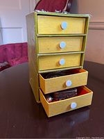 Front view of the 4-drawer yellow cardboard jewelry box with some drawers open showing contents
