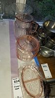 Rose-colored glass pitcher, footed covered glass bowl, divided serving dish, and a clear glass serving tray arranged on a table.