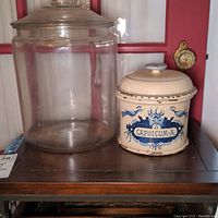 Shows large clear glass canister next to smaller ceramic crock with lid labeled 'Capsicum-A' and blue decoration.