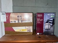 Photo showing boxed Marielle Model 46-MOBC faucet set and boxed Home Decorators Collection small exterior LED wall lantern on wooden surface.
