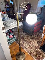 Full view of the brass toned floor lamp with illuminated globe shade showing height and main features.