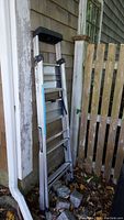 Collapsed 5 foot aluminum Gorilla ladder leaning against worn outdoor wall and wooden fence, showing overall condition.