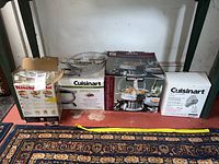 Front view of all kitchen appliance boxes on shelf including Cuisinart mixer, Kirkland chafing dish, electric fondue and KitchenAid pasta roller.