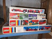 Stack of vintage model kits and LEGO sets showing box artwork of a red classic car, a plane, and LEGO houses and vehicles