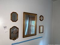 Wide view showing all five mirrors mounted on a white wall, styles varying from rectangular, octagonal, and round, mostly gold-toned frames.