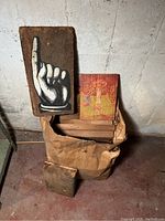 A group of weathered wood blocks placed on the floor including a large wood block with a pointing hand illustration and a smaller block with red and yellow imagery, some blocks inside a paper bag.
