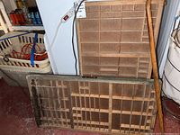 One image showing a large wooden printer's drawer and a smaller wooden printer's drawer leaning against a wall with a wooden cane on the right side.