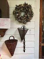 Full view of the leafy wreath, metal umbrella-shaped wall pocket with sleigh bells, and wicker wall pocket