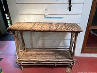 Front view of a rustic table made from natural twigs and branches showing the twig-framed body and slatted upper and lower shelves.