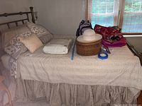 Photo of full twin bed with bedspread, skirt, pillows, folded sheets, and hat on top