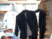 Black velvet women's blazer hanging on green hanger with visible fabric loop buttons near a children's light blue pinstripe blazer.