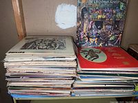 View of large stack of vintage vinyl record albums showing various well-worn sleeves and edges.